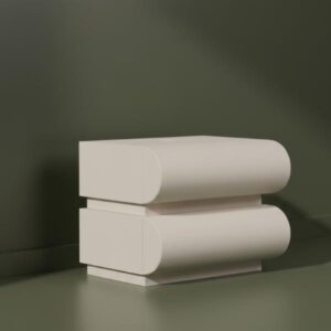 A minimalist, aesthetic view of the white, two-drawer bedside table with curved fronts. The table is presented on a surface in front of a solid dark olive green wall, with soft lighting and shadows to highlight its unique, stacked cylindrical design.