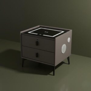 A grey/taupe colored smart bedside table with two drawers, black legs, and a black glass top with a lighted wireless charging pad, is aesthetically positioned in front of a dark olive green wall. The side panel shows a white speaker grill, and soft shadows are cast across the background.
