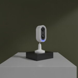 The camera is on a black rectangular block, standing on a white table, with a plain olive green background