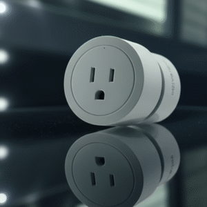 A gray, round smart plug with a US-style outlet on its front face, lying on a reflective, dark surface with a blurred background of white lights.