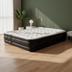 A large, black and white inflatable mattress is placed on a light wooden floor in a room featuring an olive green accent wall. A small table with a lamp sits next to the mattress, and sunlight casts a shadow of a window frame across the wall and floor, creating an aesthetic, modern interior setting.