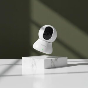 The white dome-shaped camera is levitating mid-air, rotated at a 45-degree angle, directly above a square white marble display block. The background is a dark olive green wall with soft shadows.