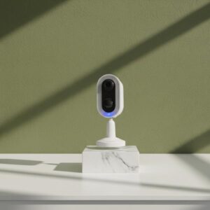 The camera is on a white marble-look block, on a white table, with an olive green background and window shadows.