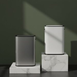 Two smart bins are displayed on two different heights of marble blocks against a dark olive green wall. The bin on the lower, smaller block is dark grey/black, while the bin on the higher, larger block is white. Both bins have dark tops. Strong shadows fall on the wall and blocks, enhancing the aesthetic contrast.