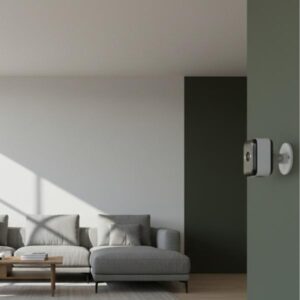 A white and black security camera is mounted on a wall column, overlooking a modern living room interior with a gray sofa and minimal decor, showcasing its use as an interior security monitor.