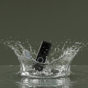 A black rectangular doorbell unit is shown splashing into water, demonstrating its water resistance. The scene has an overall olive green tone.
