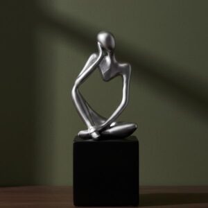 Close-up of the silver Thinking Man sculpture sitting on a black square block against a dark olive green background with sharp shadows.