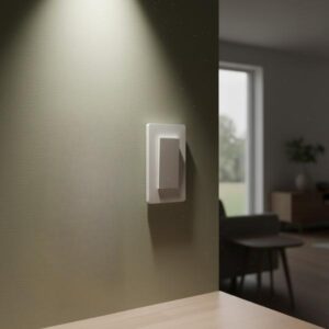 A white smart light switch is installed on a light olive green wall, above a table in a modern living room setting, highlighted by a spotlight from above.